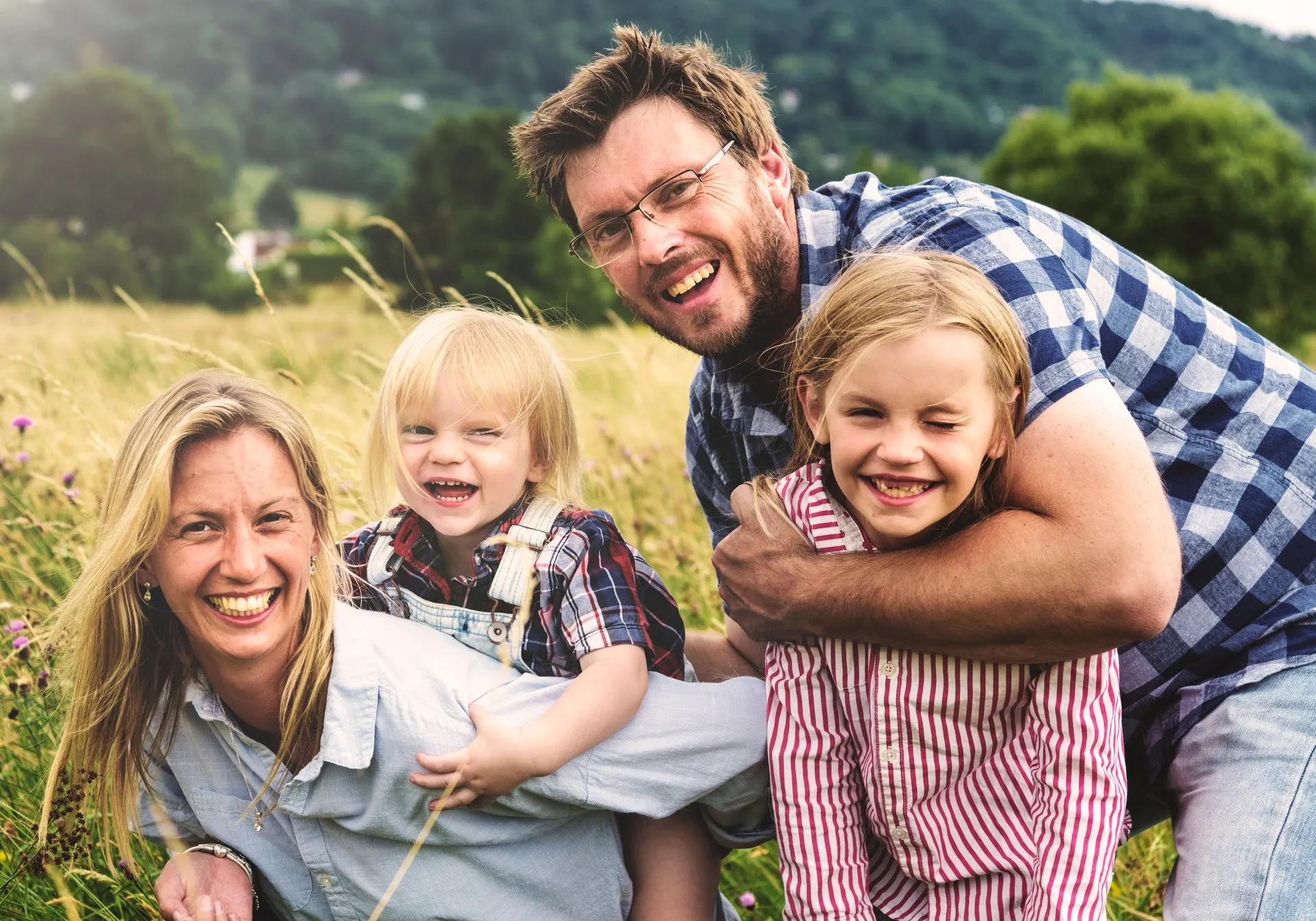 Lachende Familie mit zwei Kindern auf einer Wiese, Vater mit Brille, Mutter mit blonden Haaren.