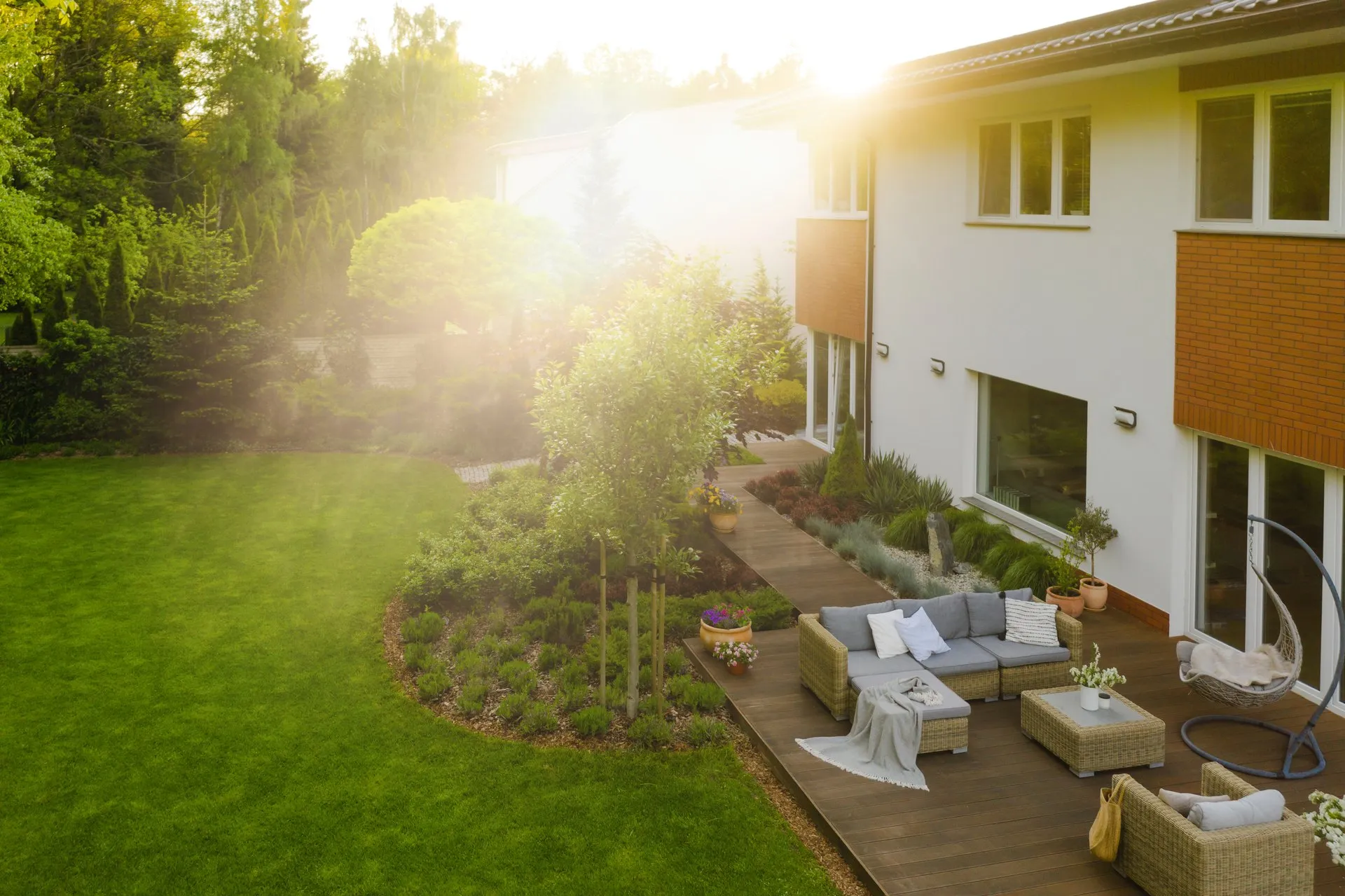 Terrasse mit Gartenmöbeln und hellem Sonnenschein neben einem modernen Haus mit Garten.
